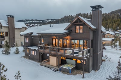 Mountain chalet with hot tub and deck nestled in snow-covered alpine setting with ski slopes nearby.