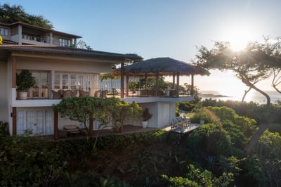 Oceanview deck with thatched lounge and glass doors glowing at dusk.
