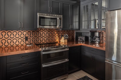 Step into your gourmet kitchen featuring sleek dark cabinetry, warm copper accents, and premium stai