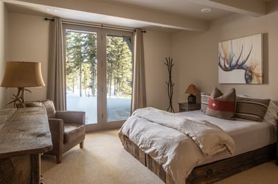 Your cozy bedroom retreat awaits with crisp linens, modern rustic decor, and snowy forest views just