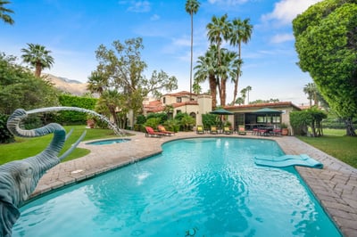 A sun-drenched backyard oasis framed by towering palms and lush greenery, featuring a sparkling pool