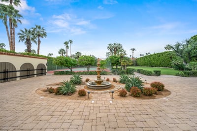 This elegant courtyard features a tiered fountain surrounded by lush landscaping, towering palm tree