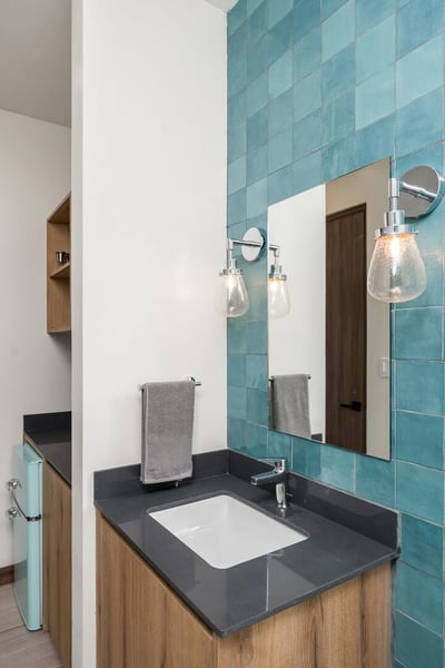- Elegant vanity with teal wall tile, dark countertop, and sleek under sink cabinet
- Globe style sc