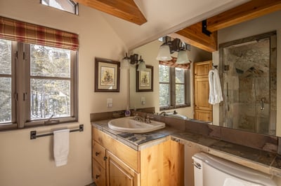 Relax in your rustic bathroom featuring warm wood beams, stone counters, and a spacious glass shower